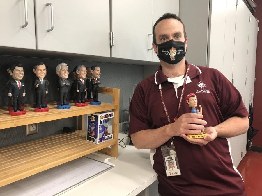 Wobble Social studies teacher Shane McBurney leans on his counter, posing with his bobbleheads and Rosie the Riveter. McBurney got his first bobblehead during his first year of teaching. 