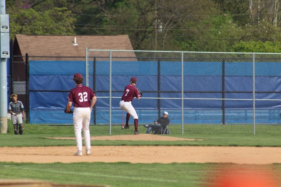 Junior Evan Alwine throws a pitch. Opposing team players on bases prepared to run. 
