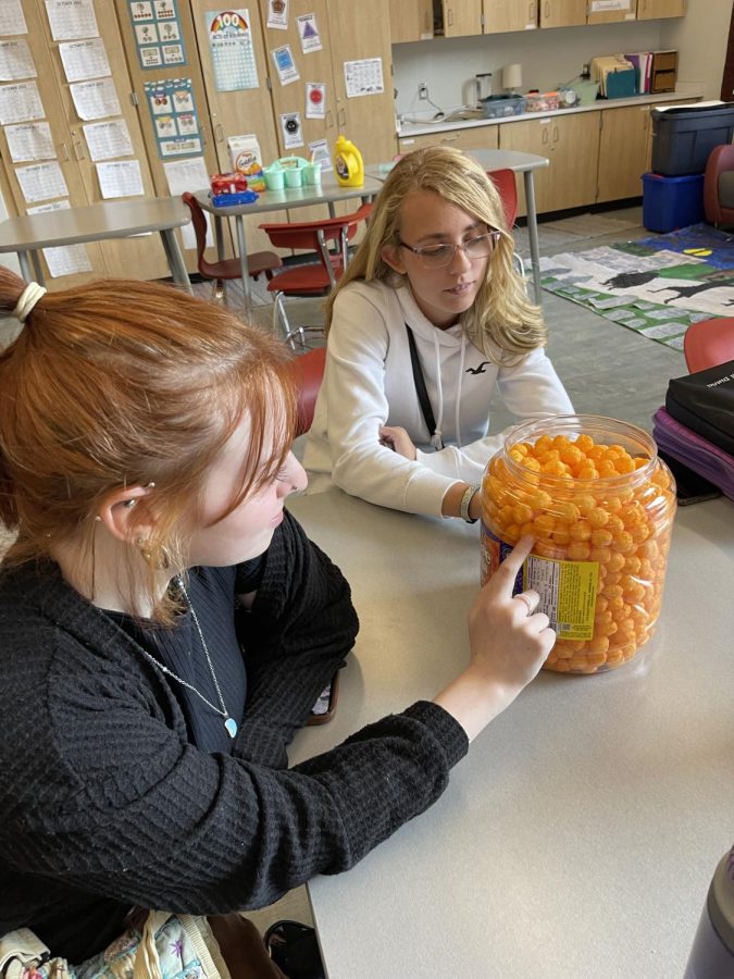 Time for a challenge. Sophomores Oriana Dent and Olivia Noel try to guess how many cheeseballs are in the container. 
