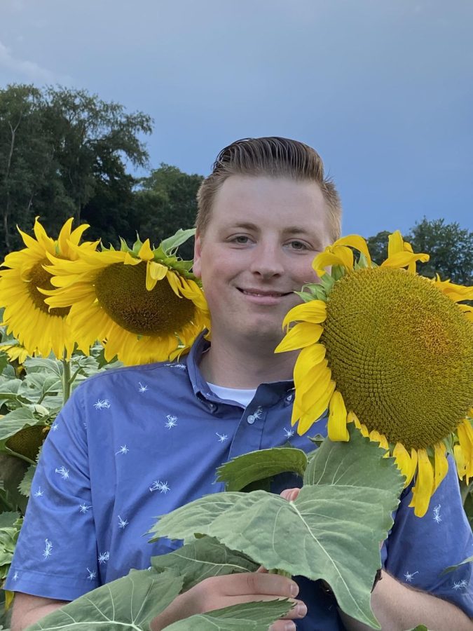 Sunshine+and+flowers.+Ninth+grade+English+teacher+Jordan+Corman+poses+with+sunflowers+to+encompass+his+bright+personality.+%0A%0A