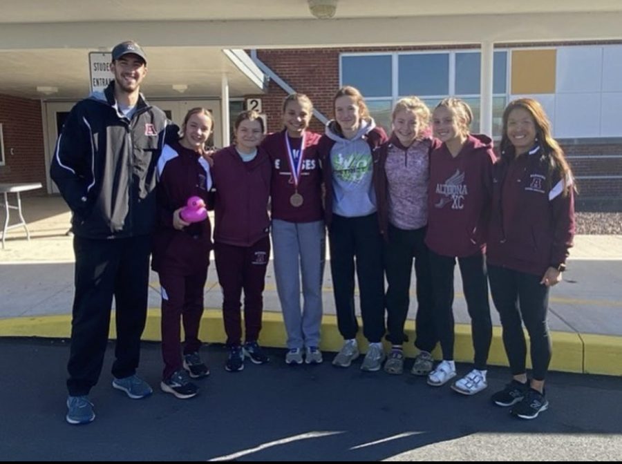 Girls cross country team in a group photo as senior Reese Wilber stands with her tenth place medal.