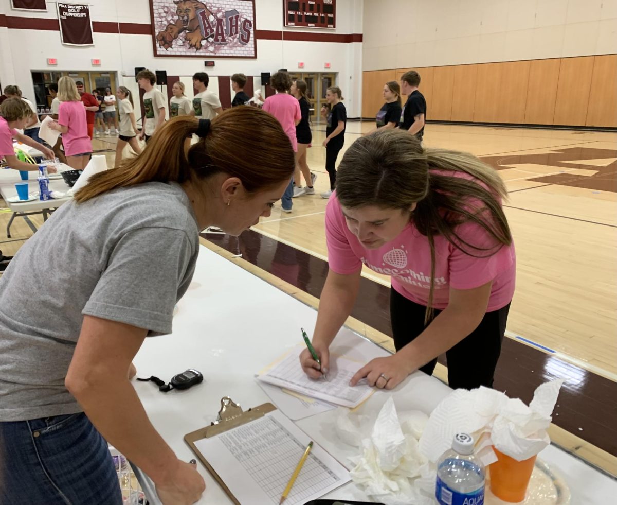 Comparing. Homecoming Committee adviser Kathryn Curry and a volunteer discuss the times for the teams and write down the winners.