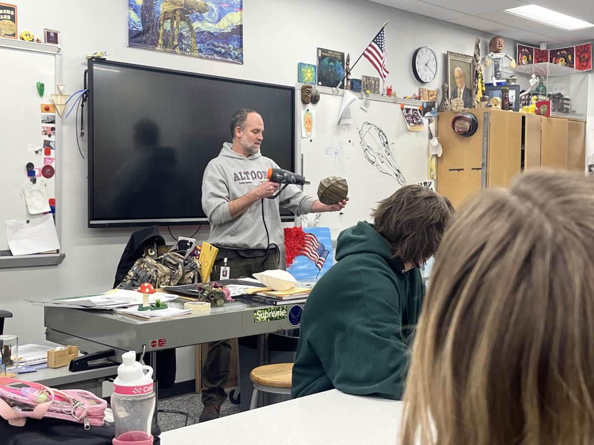 Introductions
Art teacher Eric Hoover stands in front of the class on the first day of the second semester. He is showing students how to use a heat gun to expand a work of paper mache while also explaining other procedures in the class.