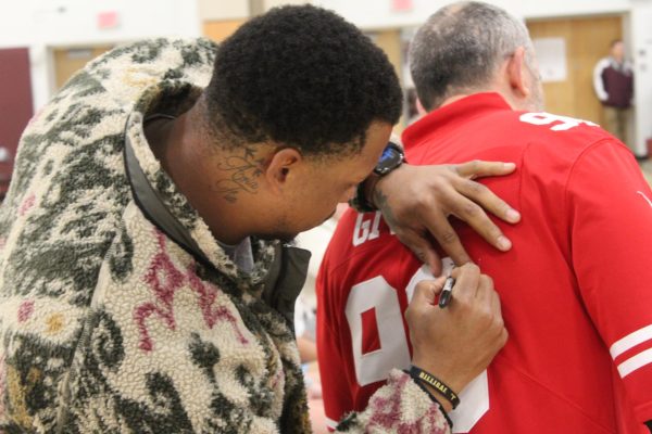 Kevin Givens signs the back of physical education teacher Tom Palfeys jersey.  Although Palfey does not collect autographed jerseys, he was excited for this particular autograph.