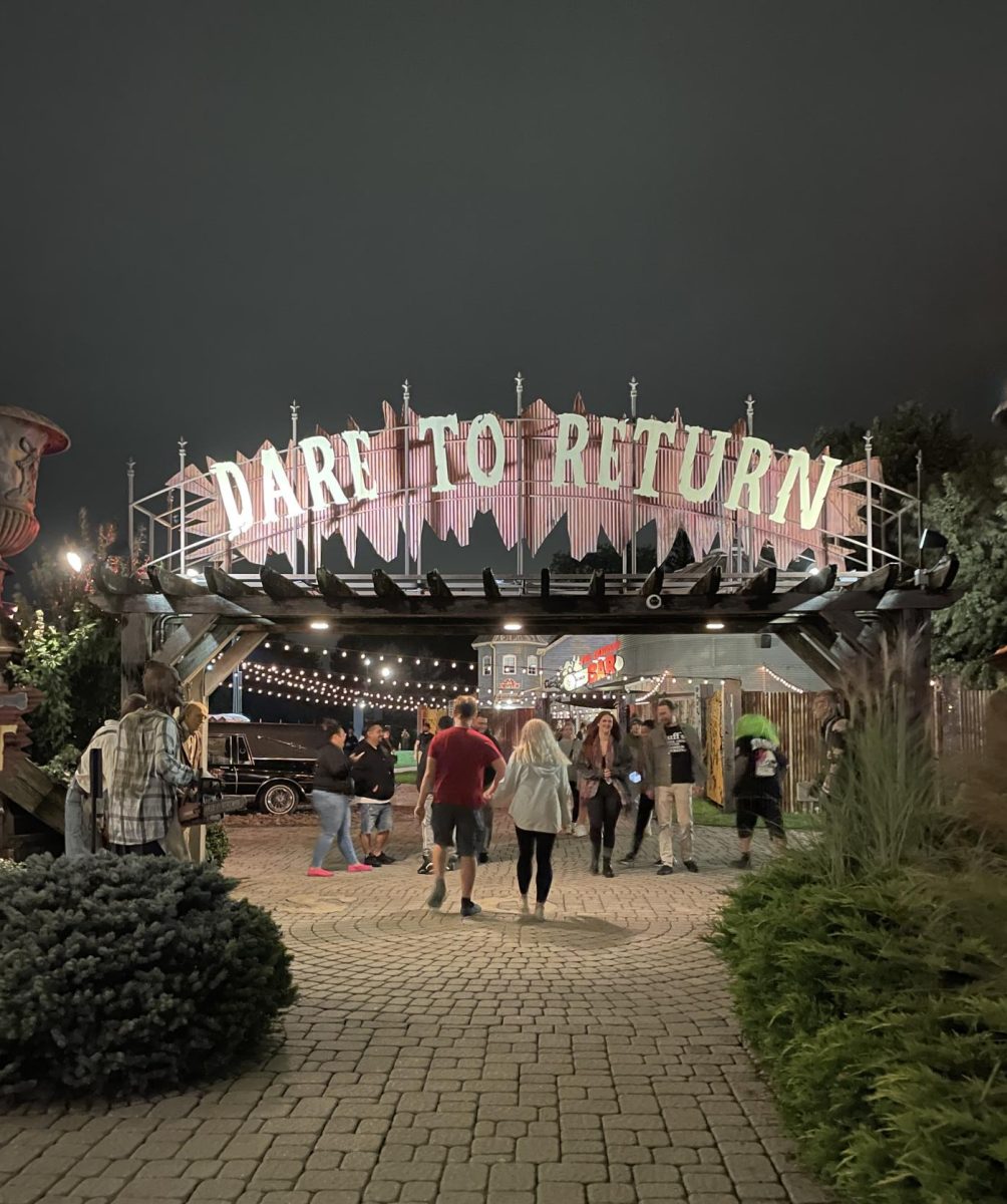 "Dare to return". Tourists walk in and out of the haunted park, passing by actors dressed as clowns and ghouls. This space under the "Field of Screams" arch can also be used for picture taking, complete with two life-like zombie mannequins.