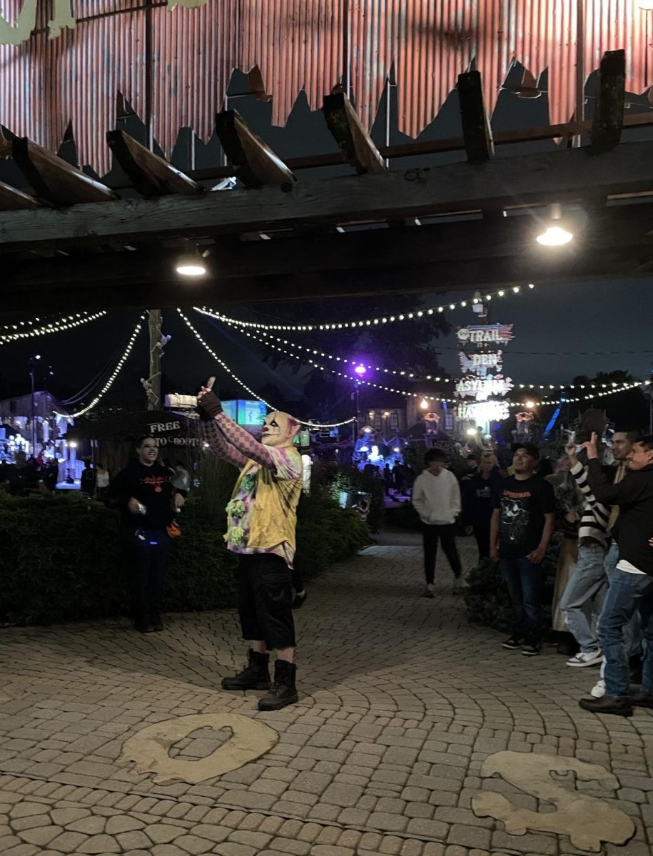 Photobomb. A worker at "Field of Screams" turns the tables on a group of people and takes a selfie instead of their group picture. At "Field of Screams" there were many actors dressed in costume walking around ready to scare passersby. 