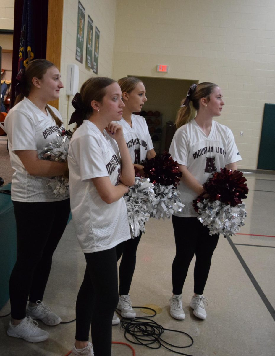 Anticipation. Cheerleaders look out at the elementary football players huddled to reveal the new trophy for the year. The trophy will be awarded to one of the classes. 