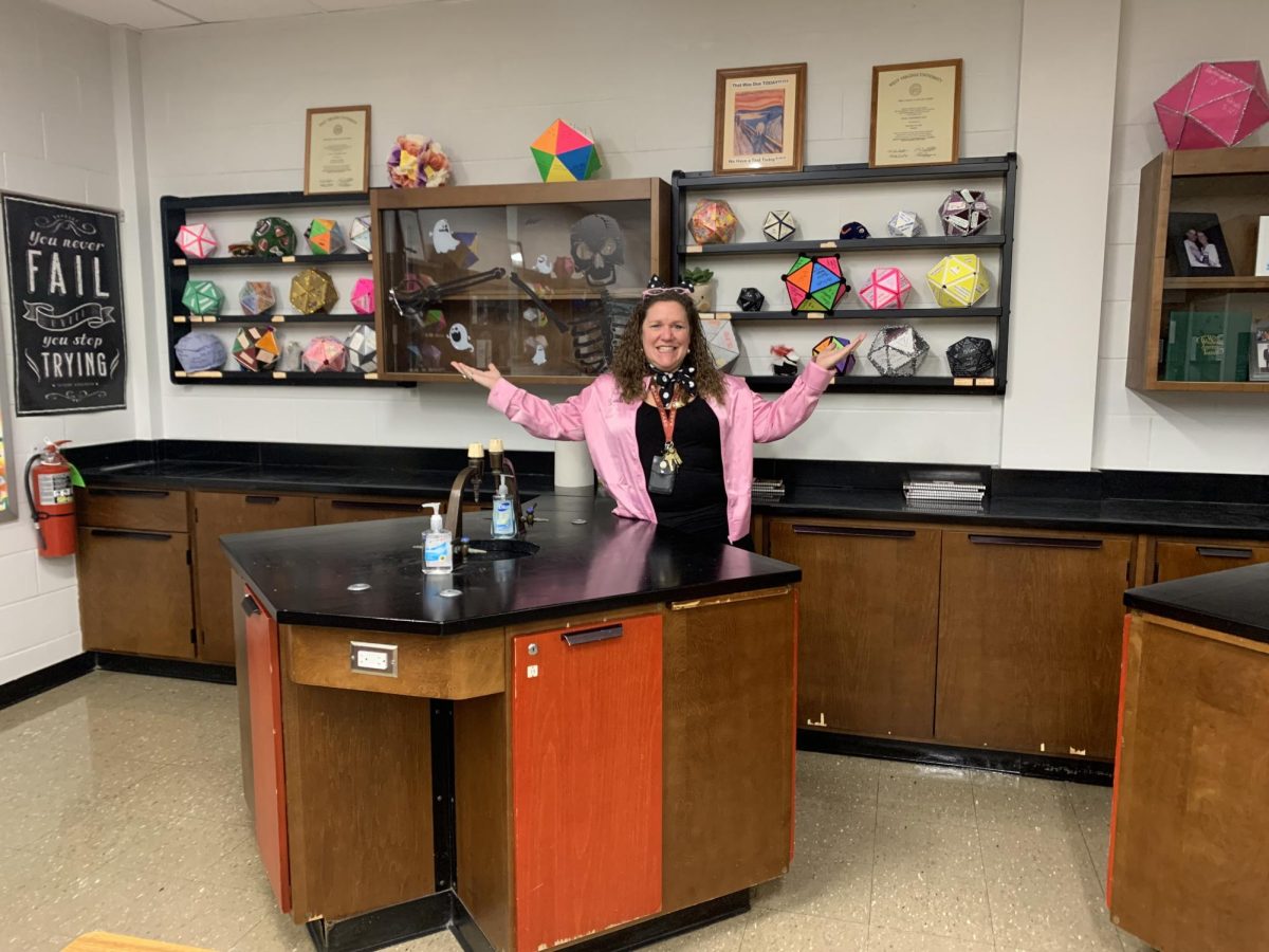 Chemistry creations. Irwin poses in her classroom with the student element icosahedron creations on her shelves. For over 20 years, she's been using this project to start off the school year in her chemistry classes. “First, students need to sign up for an element, and no two students can sign up for the same element,” Irwin said. “The last class that I teach is fifth period, so I usually wait till the end of day for them to have to come back to me to sign up, so it's first come, first serve. The kids that are really, really interested in the projects already know what element they want to do, and they're literally at my door before 2:45 and that's kind of cute, too. I give them 26 ideas. They usually just look through those. Sometimes when they're in the process of looking at the element, they find other facts that are really interesting, so they'll start researching more, and then they have to put it together.”