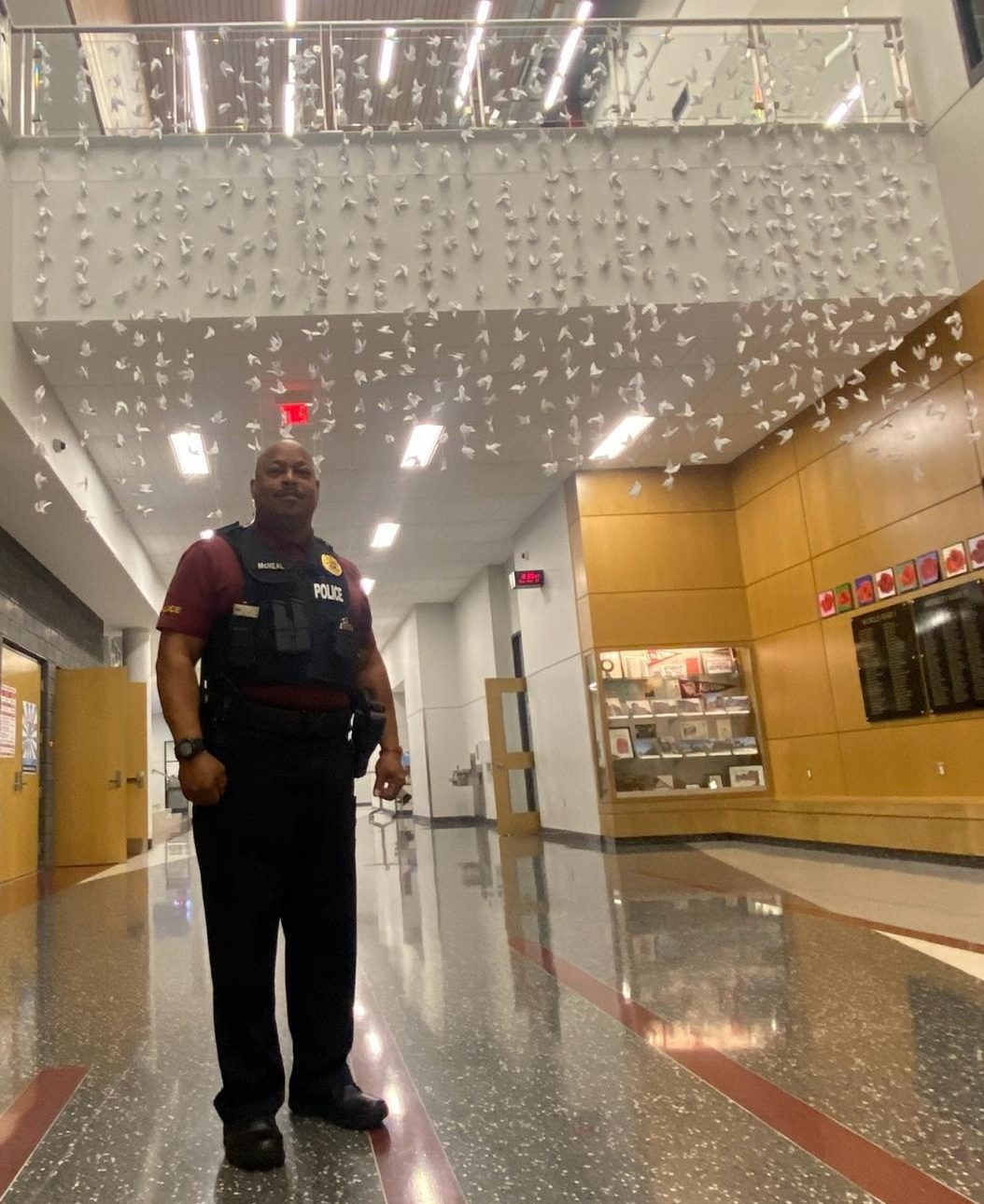 Reminders. Officer Gregory McNeal stands under origami paper birds hung on the second floor banister. Art students originally started them to honor the two students who passed away. 